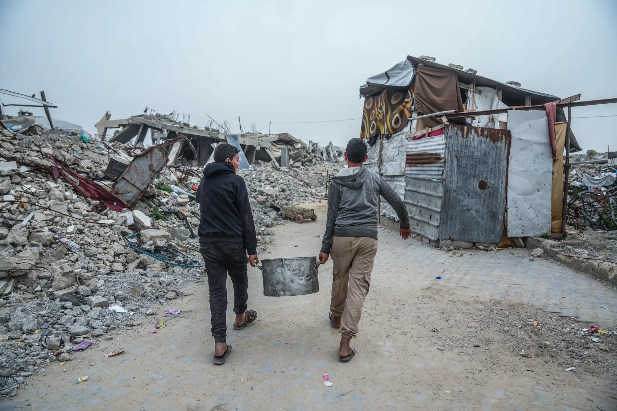 Two young men carry water through a destroyed neighbourhood in Jabaliya, Gaza. Debris clearance is helping remove barriers left by the war, making streets safer and allowing communities to reconnect with essential services as life gradually returns.