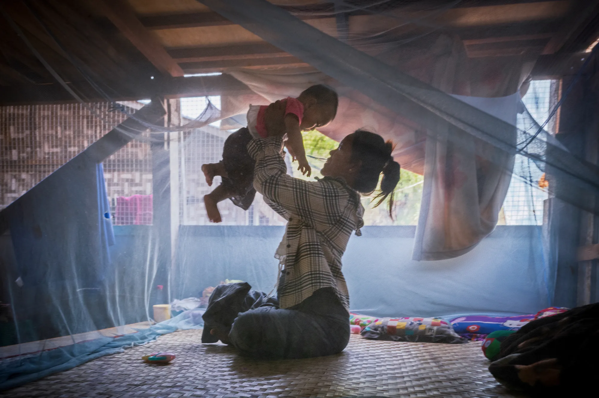 Ta Thin Nu plays with her young child inside her newly rebuilt home in Myanmar. Five months pregnant when the 2025 earthquake destroyed her house, she spent three months sleeping beneath a tree. Today, her family is home again in a safer house she designed.
